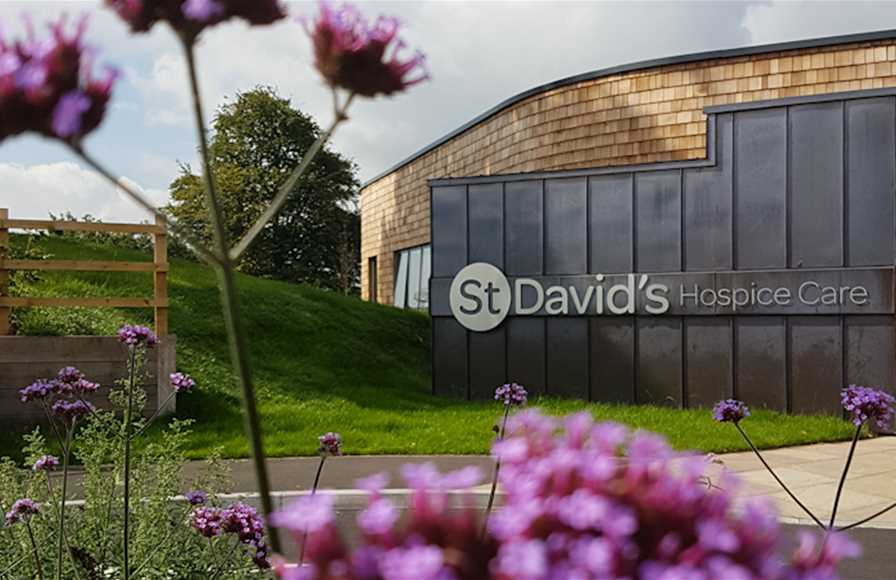 St David‘s Hospice Care In-patient unit with the signage on the front of the building, with purple flowers in a blurred out foreground.